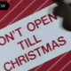 A close-up shot of a Christmas package with red paper, a green bow, and a tag reading "Don't Open Till Christmas."